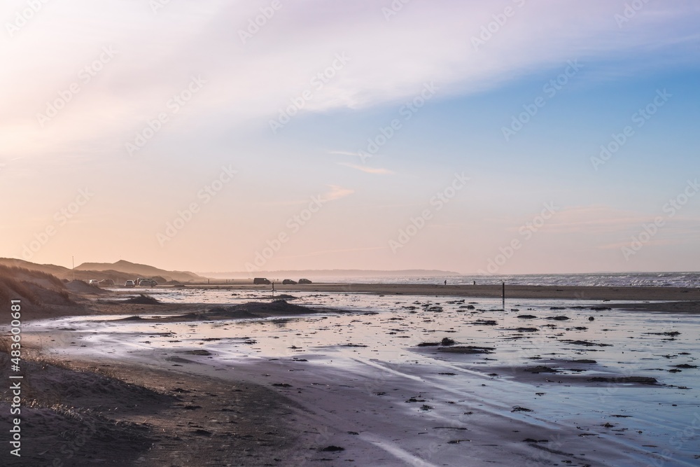 Sea water spreading on the Blokhus beach after the surf (Skagerrak, North Sea). Parked cars in the distance