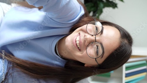 Funny caucasian teenager sitting on couch at home, using smartphone, looking at camera talking cheerfully on video call with her girl friend, sister, mother, family. vertical selfie view. 4k footage