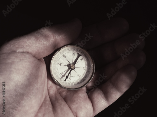 Old compass held in the palm, in semi-light. Light and shadows.