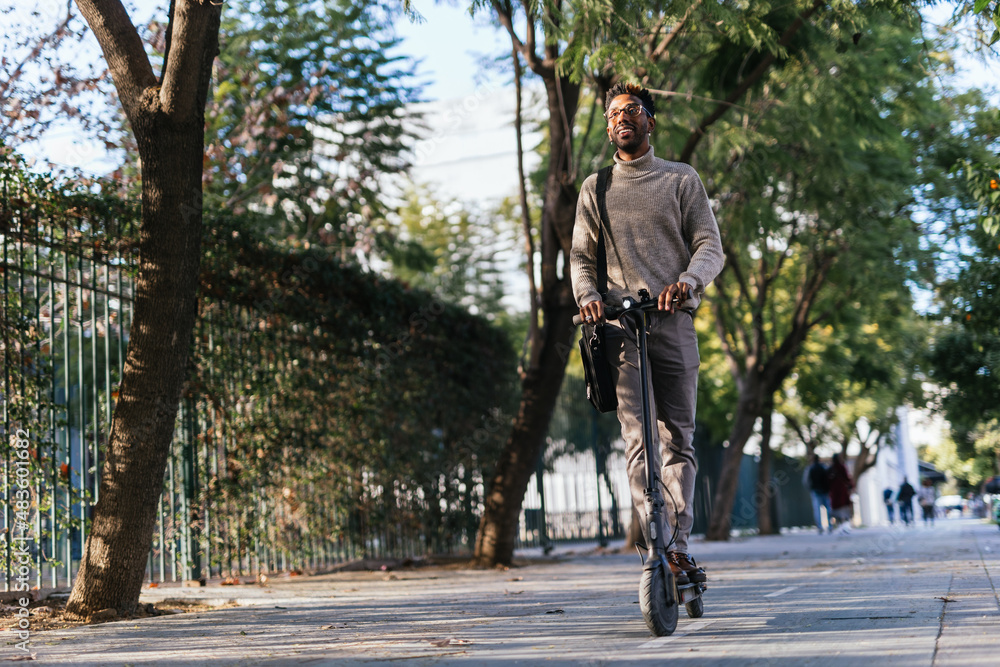 African American man smiling with high neck vest moving with his electric scooter through the city
