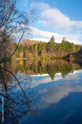 Fototapeta Naklejka Na Ścianę i Meble -  Glencoe lochan in Scottish Highlands in winter. Mirror reflection of trees, blue sky and forest in water. No people.