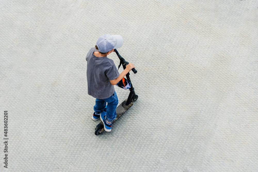 A teenager rides a scooter on a concrete surface. View from bottom to top. unrecognizable person
