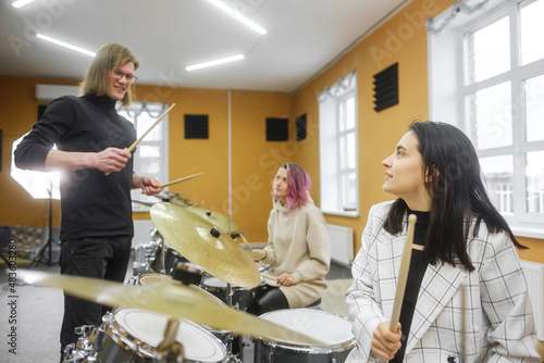 Young adult men and women learn to play drums at school. Hobbies and pastime.