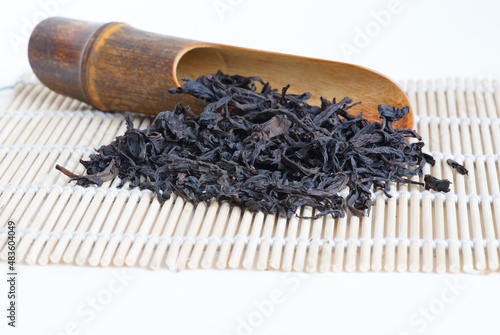 Oolong tea "Big red robe" known under original chinese name " Da hong pao  大红袍 " with wooden spoon on bamboo mat, white  background close-up, copy space, side view.