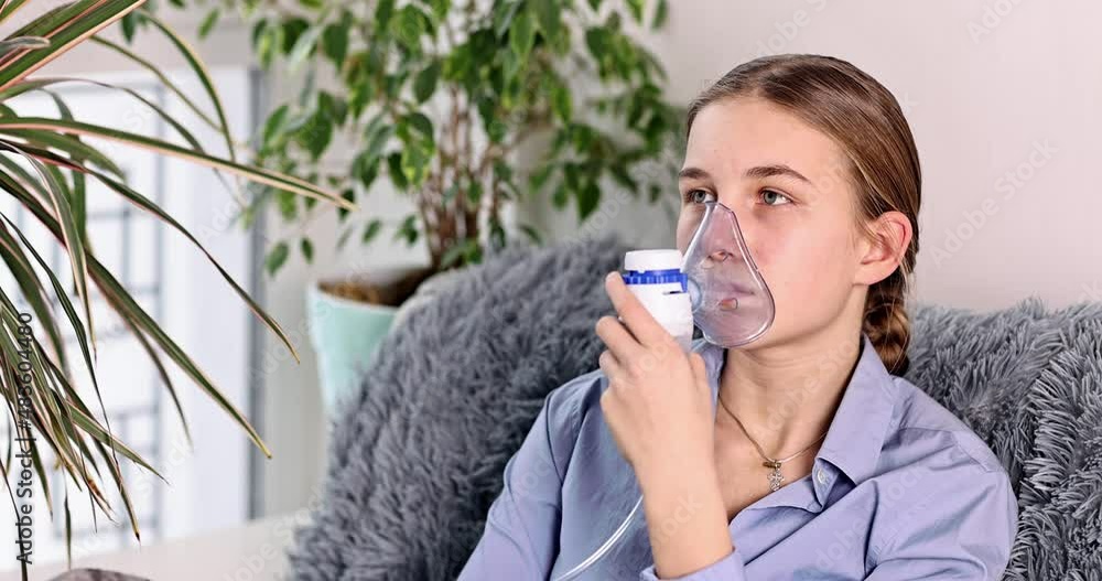 Teenage girl makes inhalation with a nebulizer equipment. Sick child holding inhalator in hand and breathes through an inhaler at home. Physical therapy for cold, flu and bronchial asthma Teenage girl makes inhalation with a nebulizer equipment. Sick child holding inhalator in hand and breathes through an inhaler at home. Physical therapy for cold, flu and bronchial asthma
