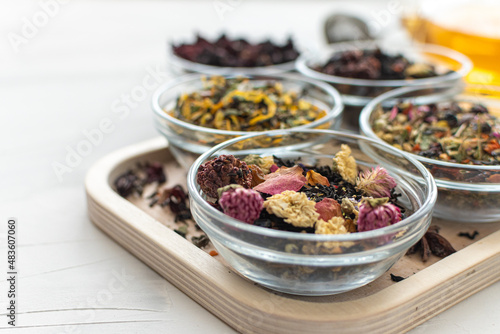 Different varieties of herbal green and black tea in glass bowls on a close-up tray. Selective focus. Herbal treatment. Healthy lifestyle. Therapeutic aromatic and delicious drinks. Space for text.