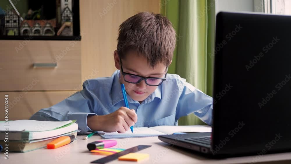 distance learning. a teenage student is studying on a laptop. writing down a synopsis in a notebook. sitting at home at the writing desk distance learning. a teenage student is studying on a laptop. writing down a synopsis in a notebook. sitting at home at the writing desk