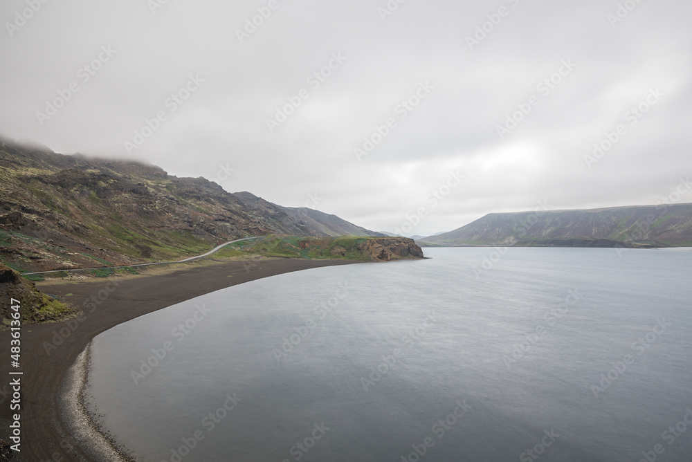 Mountain lake in Iceland on a cloudy summer day. A winding road runs along the side of the lake.