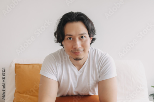 Happy smile face of long hair Asian man sit on the sofa in living room.