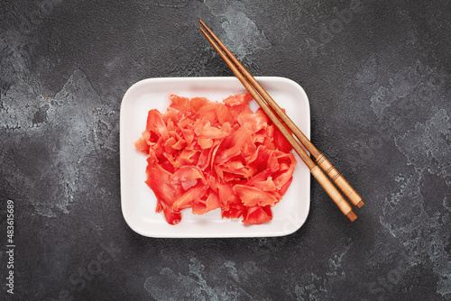 Red pickled ginger on a white porcelain plate with chopsticks on a black textured background. Natural ingredient of Oriental cuisine. A product that increases immunity. Flat lay