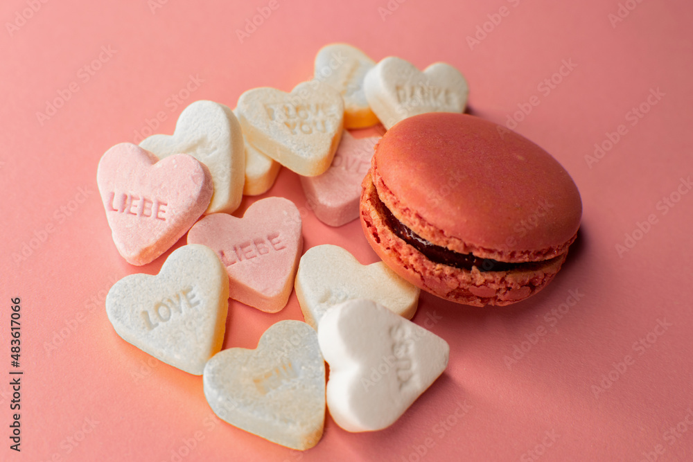 Pinker Macaron auf rosa Grund mit Liebes-Süßigkeiten. Pink macaron on rosé ground with love-candy. Pinker Macaron auf rosa Grund mit Liebes-Süßigkeiten. Pink macaron on rosé ground with love-candy.