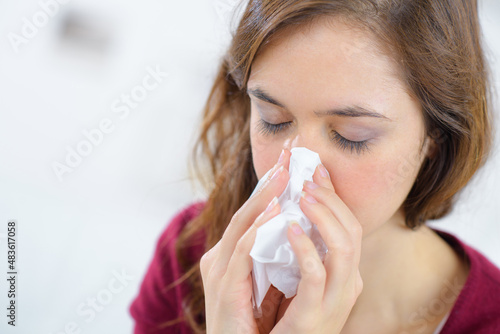 young woman blowing nose on tissue against white background