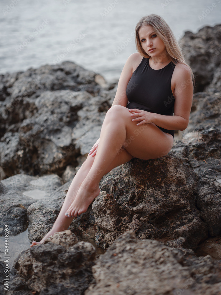 Portrait of attractive blonde woman with long hair posing on rocky beach.