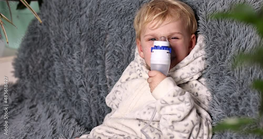 Cute baby boy makes inhalation with a nebulizer equipment. Sick child holding inhalator in hand and breathes through an inhaler at home. Physical therapy for cold, flu and bronchial asthma Cute baby boy makes inhalation with a nebulizer equipment. Sick child holding inhalator in hand and breathes through an inhaler at home. Physical therapy for cold, flu and bronchial asthma