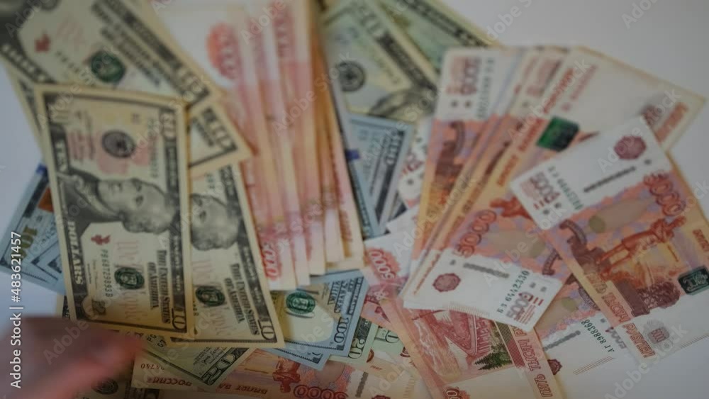Two hands take turns throwing Russian and American bills onto the white table. The hand throws five thousandth bills. Hand throwing one hundred dollar and twenty dollar bills Two hands take turns throwing Russian and American bills onto the white table. The hand throws five thousandth bills. Hand throwing one hundred dollar and twenty dollar bills