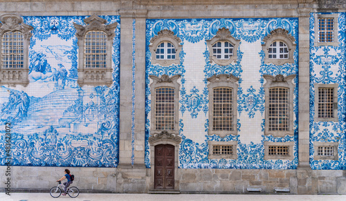 Carmo church in Porto, Portugal, decorated with blue tiles - Traveler woman cycling next to the painted ceramic wall in the old town of Oporto. photo