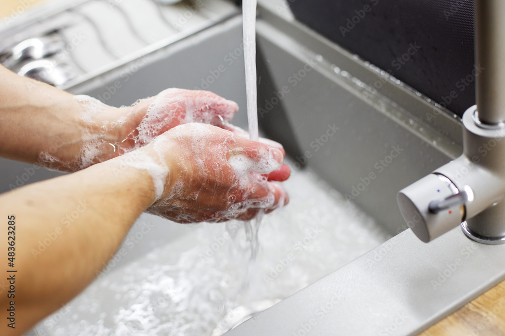 Fototapeta premium A man washes his hands with soap under the tap under running water close-up. Health, and hygiene concept.