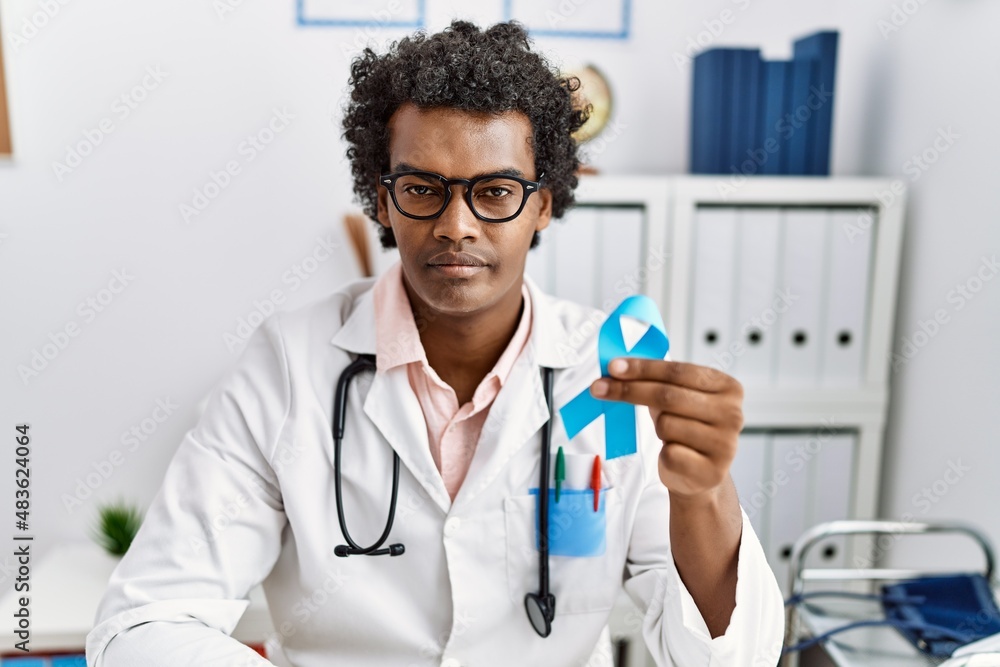 African doctor man holding blue ribbon thinking attitude and sober expression looking self confident African doctor man holding blue ribbon thinking attitude and sober expression looking self confident