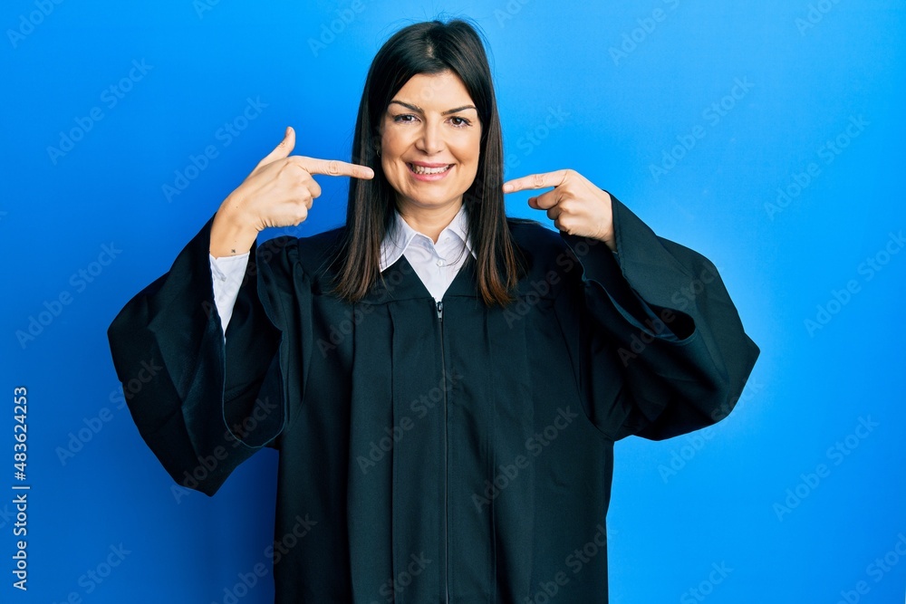 Young hispanic woman wearing judge uniform smiling cheerful showing and pointing with fingers teeth and mouth. dental health concept. Young hispanic woman wearing judge uniform smiling cheerful showing and pointing with fingers teeth and mouth. dental health concept.