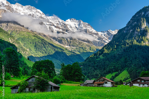 village in the swiss alps on a summer day, with snowy mountains in the background - switzerland.
