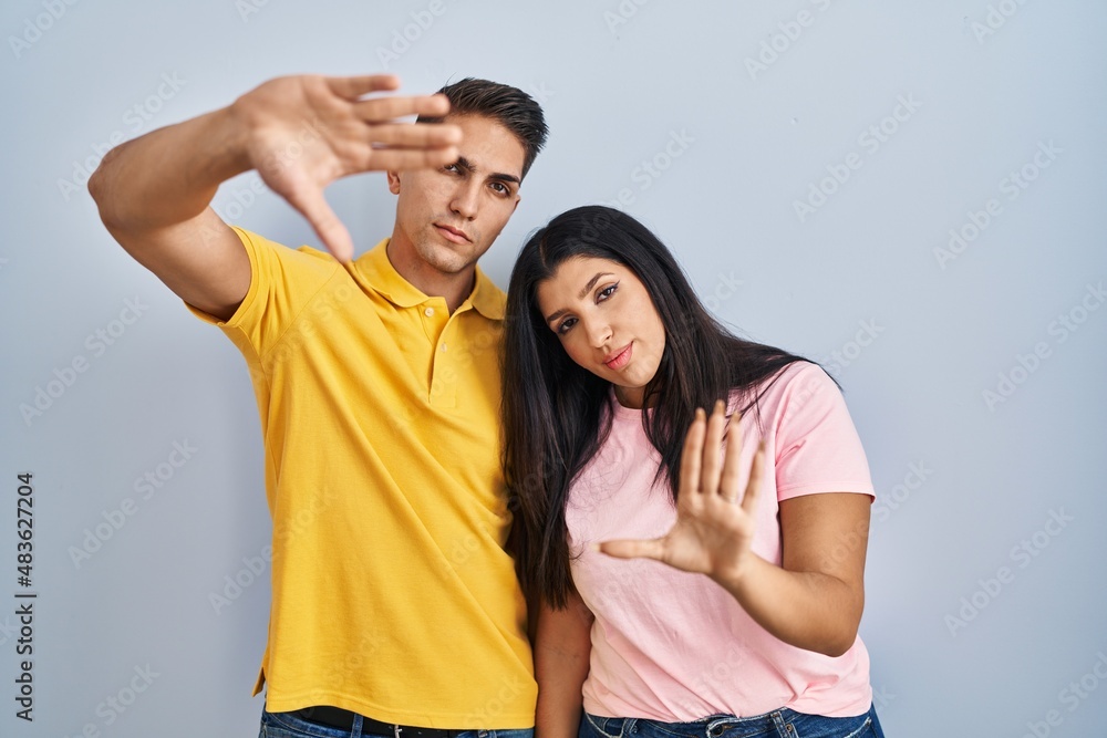 Fototapeta premium Young couple standing over isolated background doing frame using hands palms and fingers, camera perspective