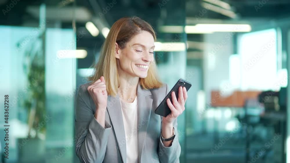 Excited business woman rejoices at message on her use smartphone. Happy cheerful joyful glad female manager in formal suit looking at mobile phone celebrate good news victory success in office success Excited business woman rejoices at message on her use smartphone. Happy cheerful joyful glad female manager in formal suit looking at mobile phone celebrate good news victory success in office success