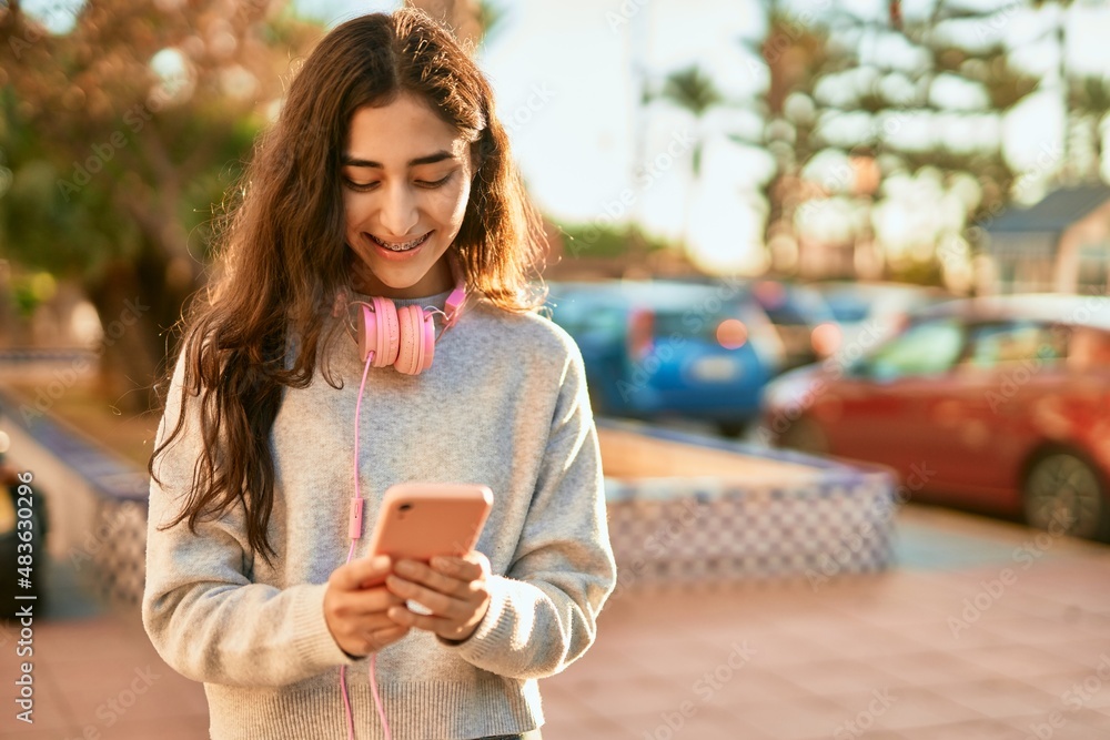 Young middle east girl smiling happy using smartphone and headphones at the city. Young middle east girl smiling happy using smartphone and headphones at the city.