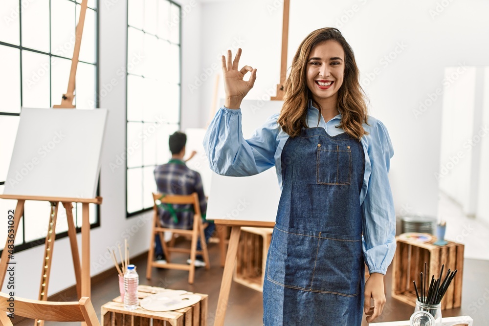 Young artist woman at art studio smiling positive doing ok sign with hand and fingers. successful expression. Young artist woman at art studio smiling positive doing ok sign with hand and fingers. successful expression.
