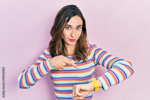 Young hispanic girl wearing casual clothes in hurry pointing to watch time, impatience, upset and angry for deadline delay photo