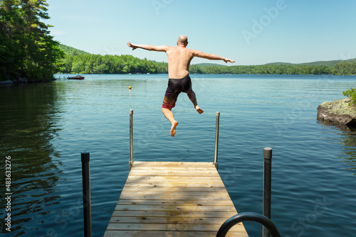 Happy man jumping off dock into lake the summer time. Having fun on vacation.