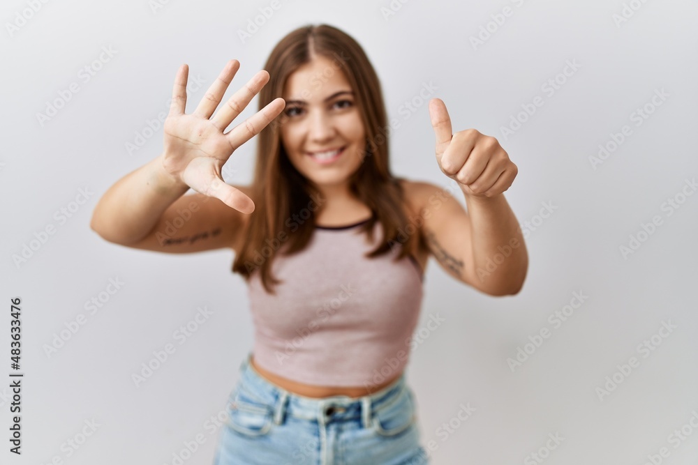 Young brunette woman standing over isolated background showing and pointing up with fingers number six while smiling confident and happy. Young brunette woman standing over isolated background showing and pointing up with fingers number six while smiling confident and happy.