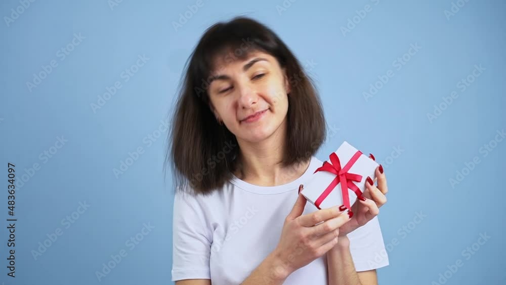 Beautiful smiling woman holding gift box in hand on blue wall background. Girl is happy with present Beautiful smiling woman holding gift box in hand on blue wall background. Girl is happy with present