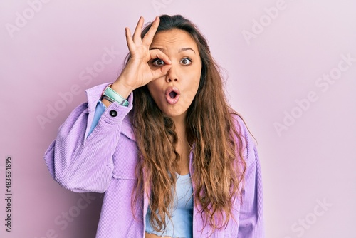Young hispanic girl wearing casual clothes doing ok gesture shocked with surprised face, eye looking through fingers. unbelieving expression. photo