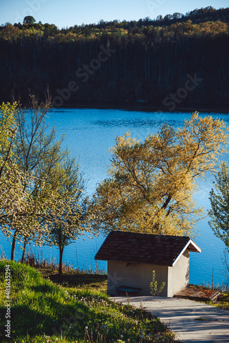 A lake with hills in the background. A little boat house on the shore of the lake. Clear blue sky. High quality photo