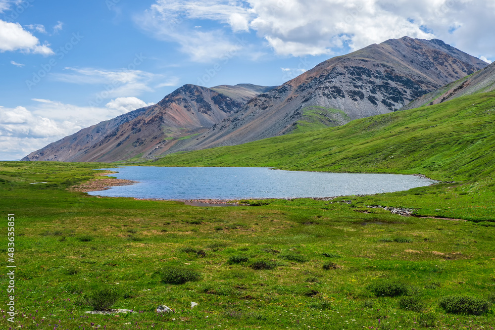Colorful summer landscape with beautiful lake in sunlit green mountain valley among rocks and high mountain ridge under blue sky. Awesome scenery with alpine lake among greenery in sunlight. Colorful summer landscape with beautiful lake in sunlit green mountain valley among rocks and high mountain ridge under blue sky. Awesome scenery with alpine lake among greenery in sunlight.