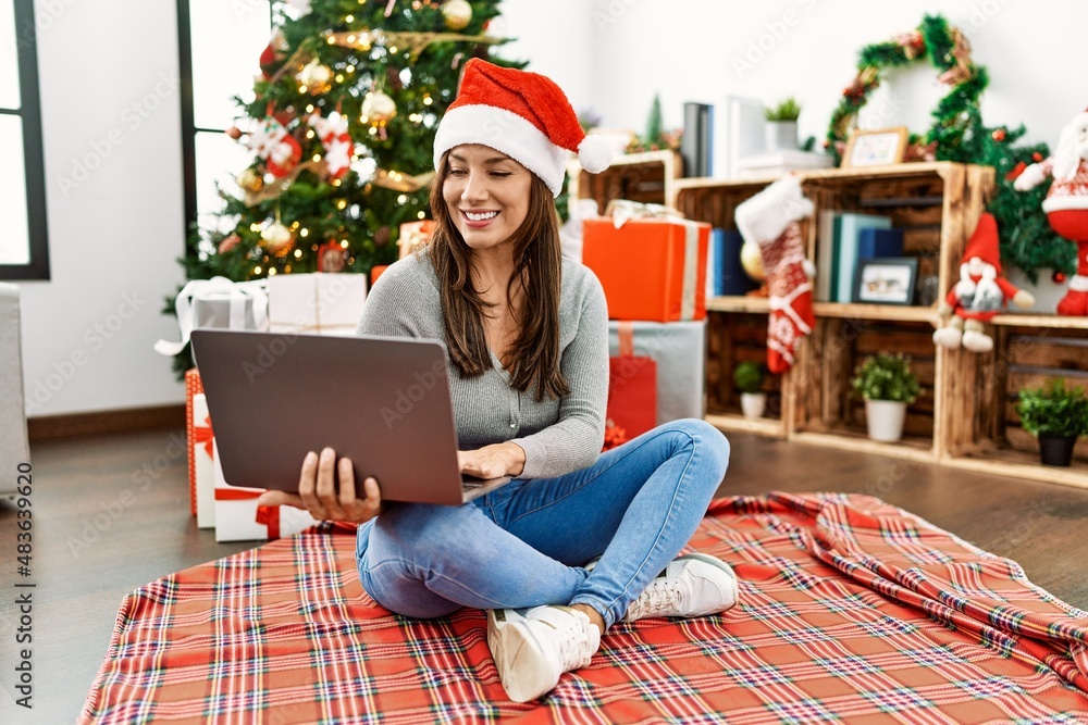Young latin woman using laptop sitting by christmas tree at home Young latin woman using laptop sitting by christmas tree at home