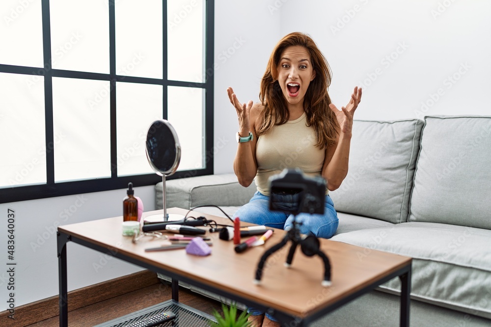 Middle age hispanic woman recording make up tutorial with smartphone at home crazy and mad shouting and yelling with aggressive expression and arms raised. frustration concept. Middle age hispanic woman recording make up tutorial with smartphone at home crazy and mad shouting and yelling with aggressive expression and arms raised. frustration concept.