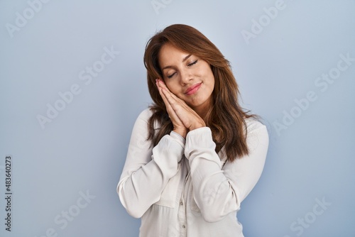 Hispanic woman standing over isolated background sleeping tired dreaming and posing with hands together while smiling with closed eyes.