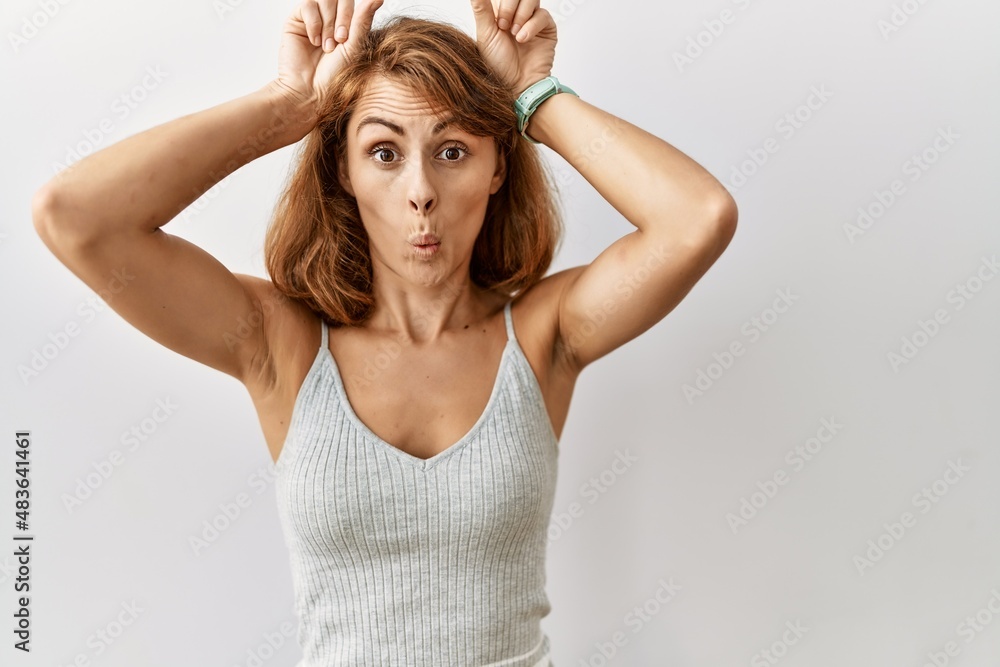 Beautiful caucasian woman standing over isolated background doing funny gesture with finger over head as bull horns Beautiful caucasian woman standing over isolated background doing funny gesture with finger over head as bull horns