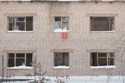 Фасад заброшенного кирпичного дома с распахнутыми и выбитыми окнами