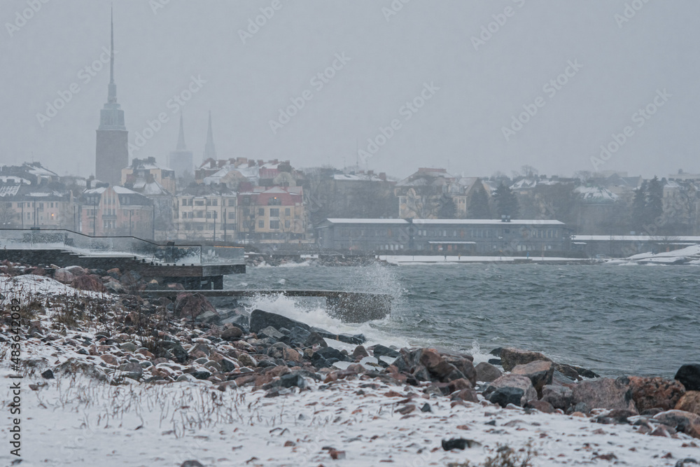 View of Helsinki from the seashore in a winter storm, waves breaking on a rocky shore. Finland weather..