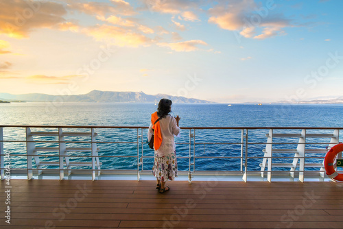 Foto A woman stands on the deck of a cruise ship at sunset while it cruises the Mediterranean sea surrounded by Greek Islands