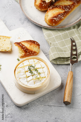 Oven baked camembert cheese with lye baguette bread on marble board, grey concrete surface. Homemade grilled brie with thyme on green checkered kitchen towel