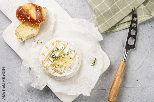 Oven baked camembert cheese with lye baguette bread on marble board, grey concrete surface. Homemade grilled brie with thyme on green checkered kitchen towel