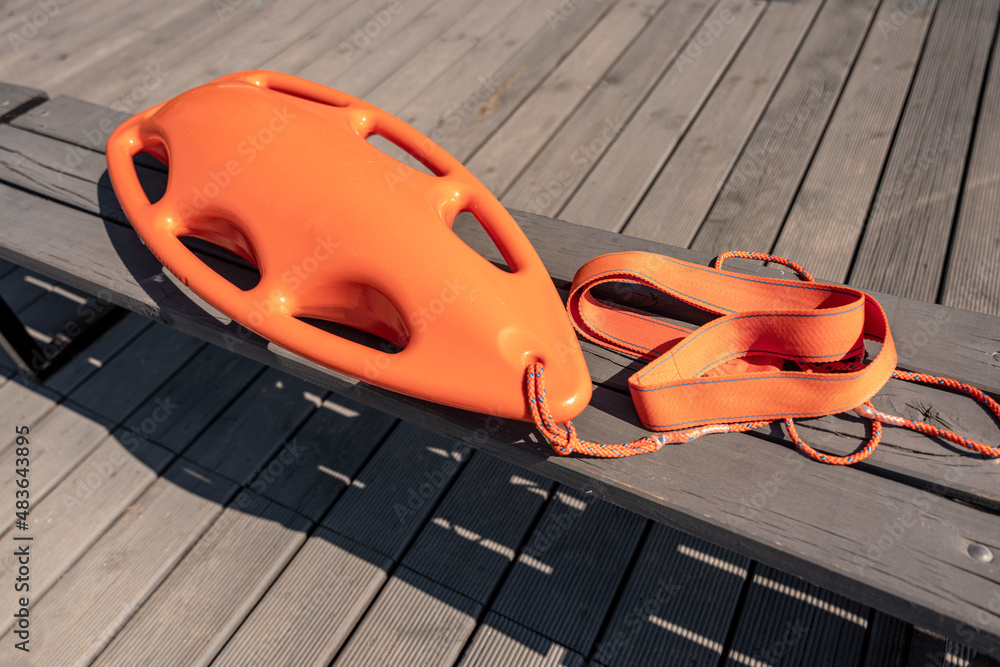 Podstawowe wyposażenie ratownika wodnego w kolorze pomarańczowym. Pomaga w utrzymaniu się na wodzie podczas udzielania pomocy. Ratownicy posiadają taki sprzęt zarówno na akwenach morskich jak i jezior - obrazy, fototapety, plakaty 