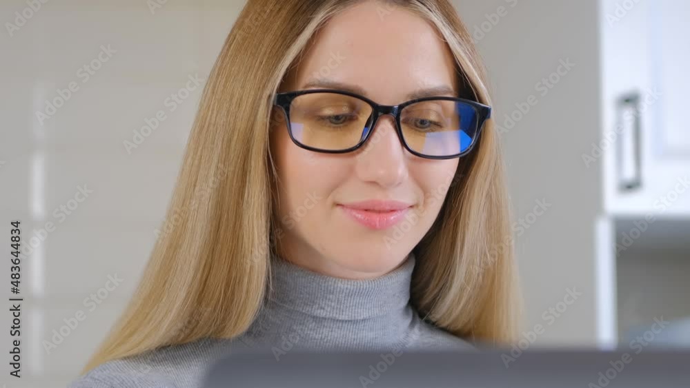 Happy white woman working on computer. Video portrait of beautiful young adult female with long blonde hair wearing glasses, doing distant work on laptop at home during lockdown Happy white woman working on computer. Video portrait of beautiful young adult female with long blonde hair wearing glasses, doing distant work on laptop at home during lockdown