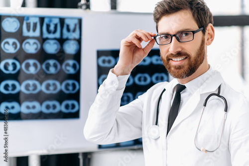 Medicine and healthcare concept. Proud smart male doctor, general medicine doctor, surgeon, radiologist, wearing glasses and medical uniform, standing in the clinic, looking at the camera, smiling