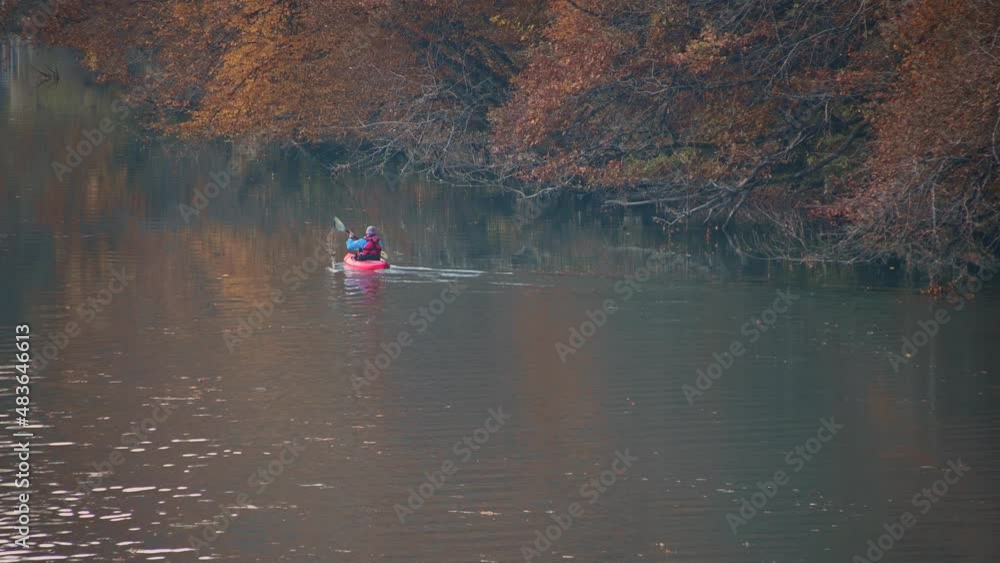 Elevated view of person kayaking on calm Sava River in Slovenia. Sailing away along the river. Banks covered with colorful trees in autumn. Real time, static shot Elevated view of person kayaking on calm Sava River in Slovenia. Sailing away along the river. Banks covered with colorful trees in autumn. Real time, static shot