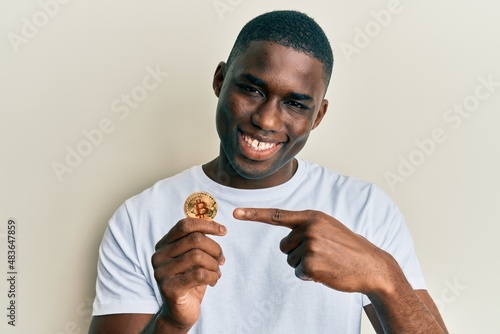 Young african american man holding virtual currency bitcoin smiling happy pointing with hand and finger