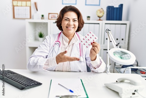 Middle age hispanic woman wearing doctor uniform holding pills at clinic